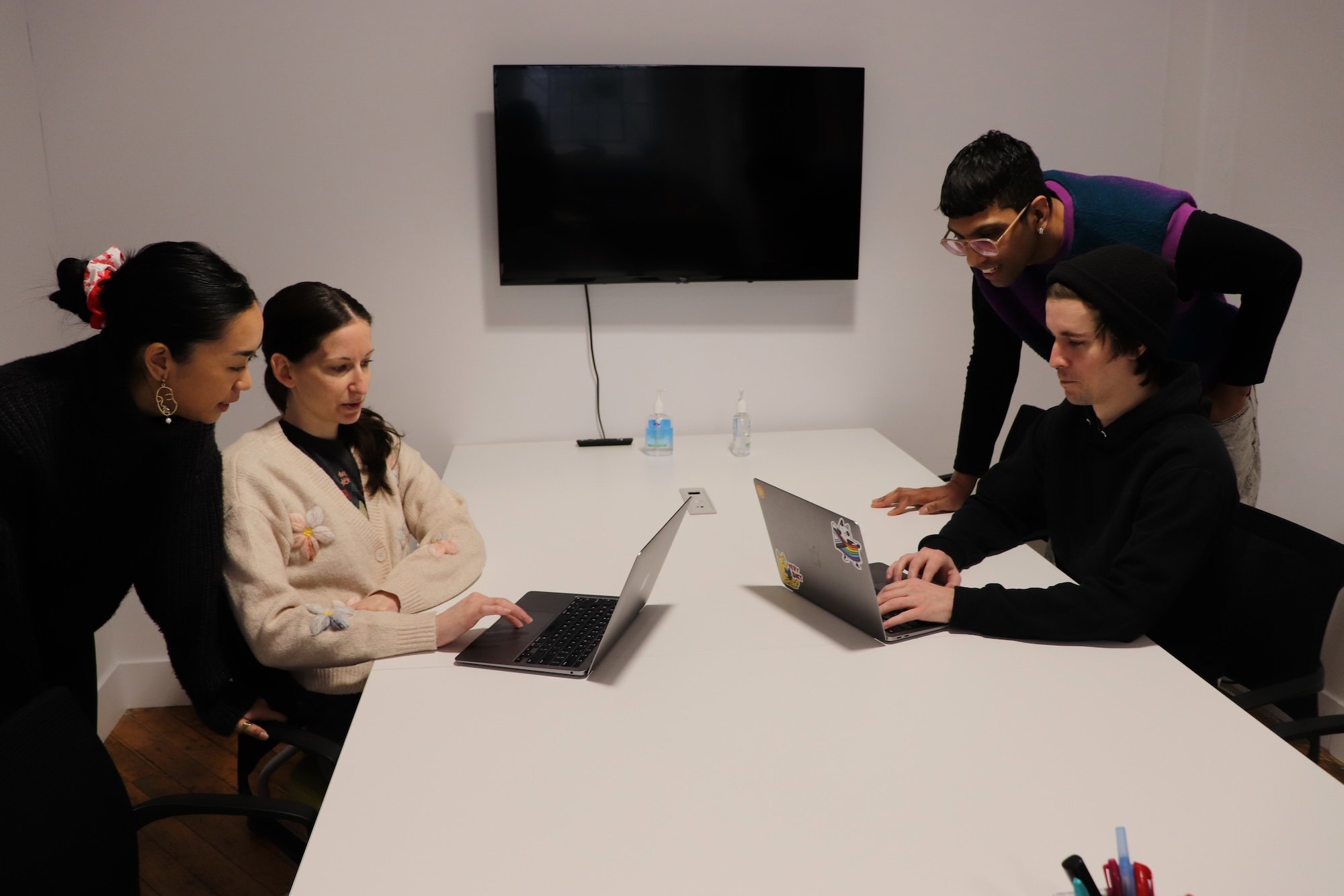 Four adults working together on two laptop computers